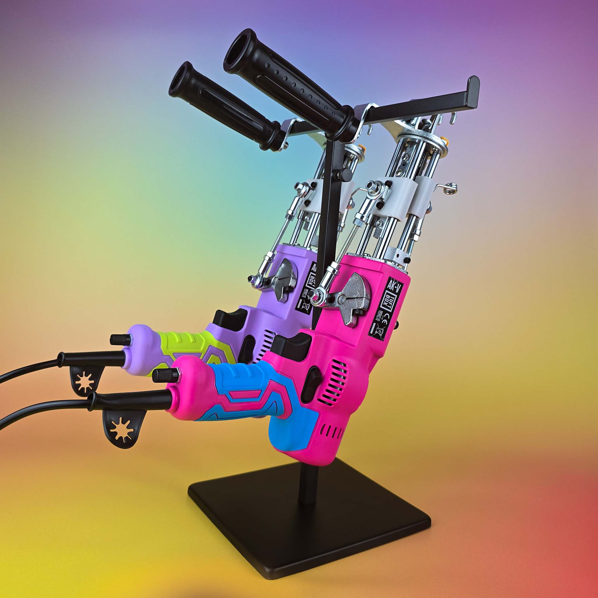 Tuftbox AK-V Rug Tufting Guns. Both Models Hanging From A Display Stand Showing Two Different Colour Varients: Purple Glow And Fire Pink