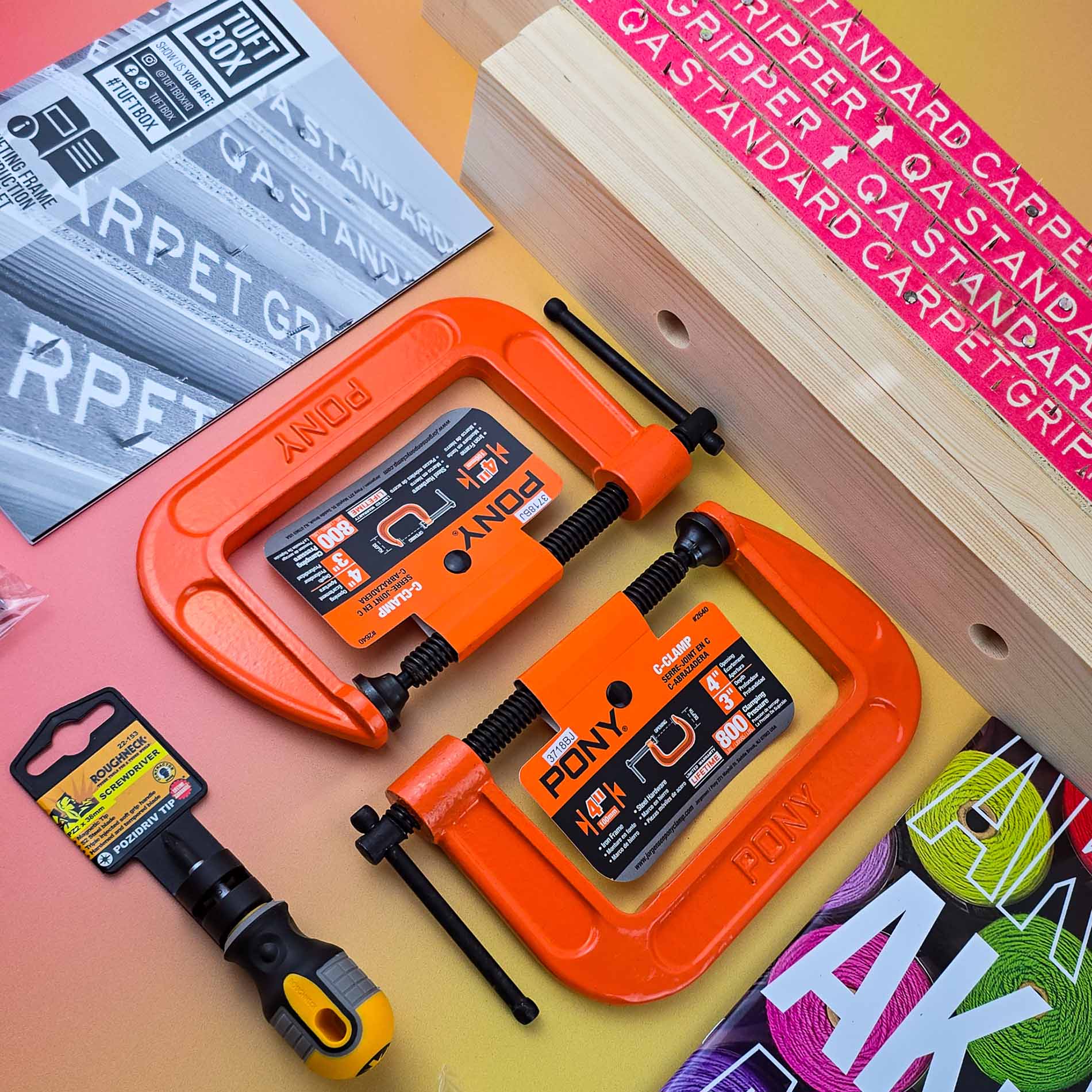 angled view of bright orange c-clamps on soft red and yellow ombre backdrop with rug tufting frame and instructions