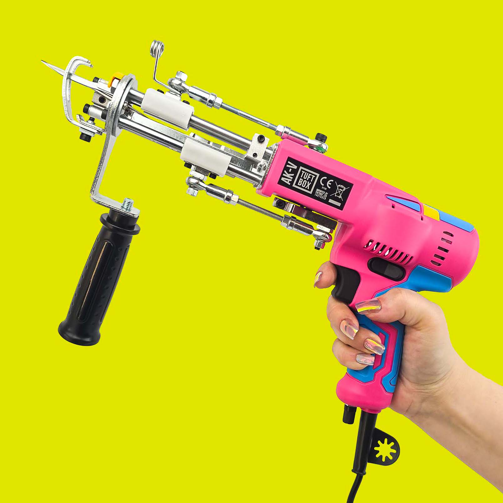 Pink and Blue AK5 rug tuft gun being held in the air by a hand with a bright green-yellow background