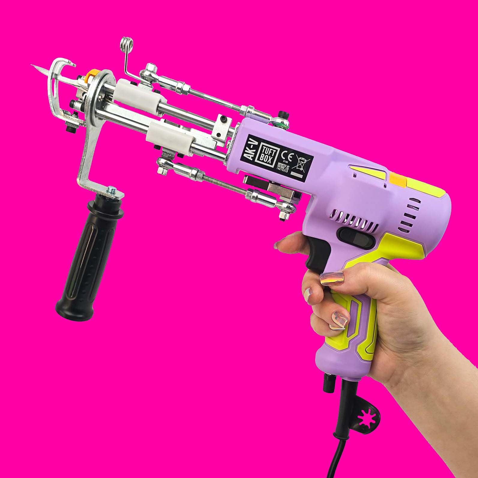 Purple and bright neon green AK-V AK5 rug tufting machine held by a hand against a bright hot pink background