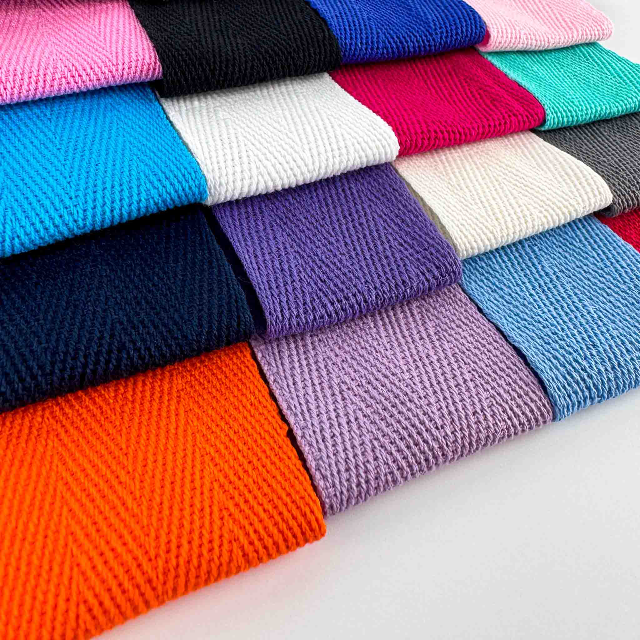 Stack of colorful folded webbing herringbone tapes on a white background