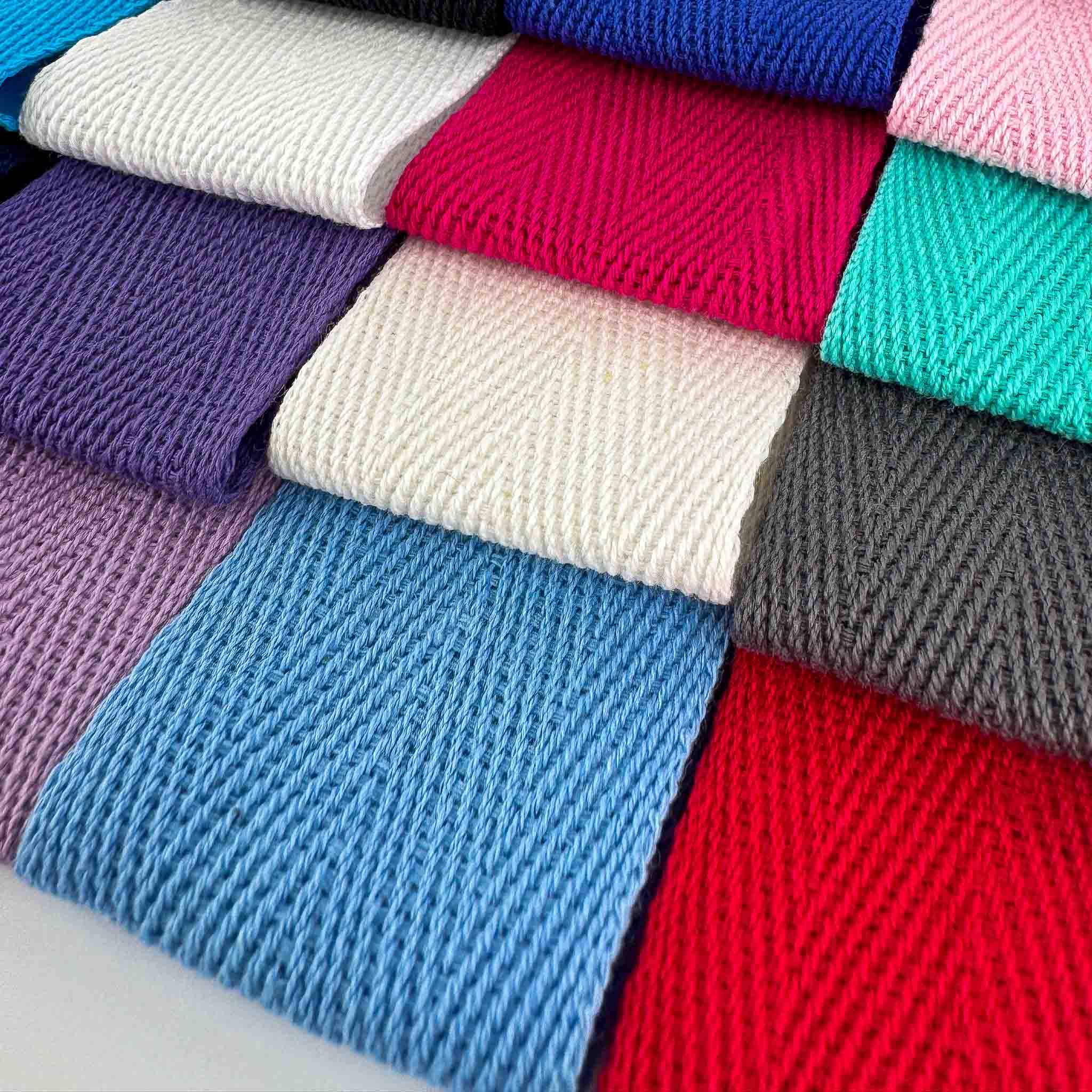 Close up of stack of colourful webbing herringbone tapes on a white background