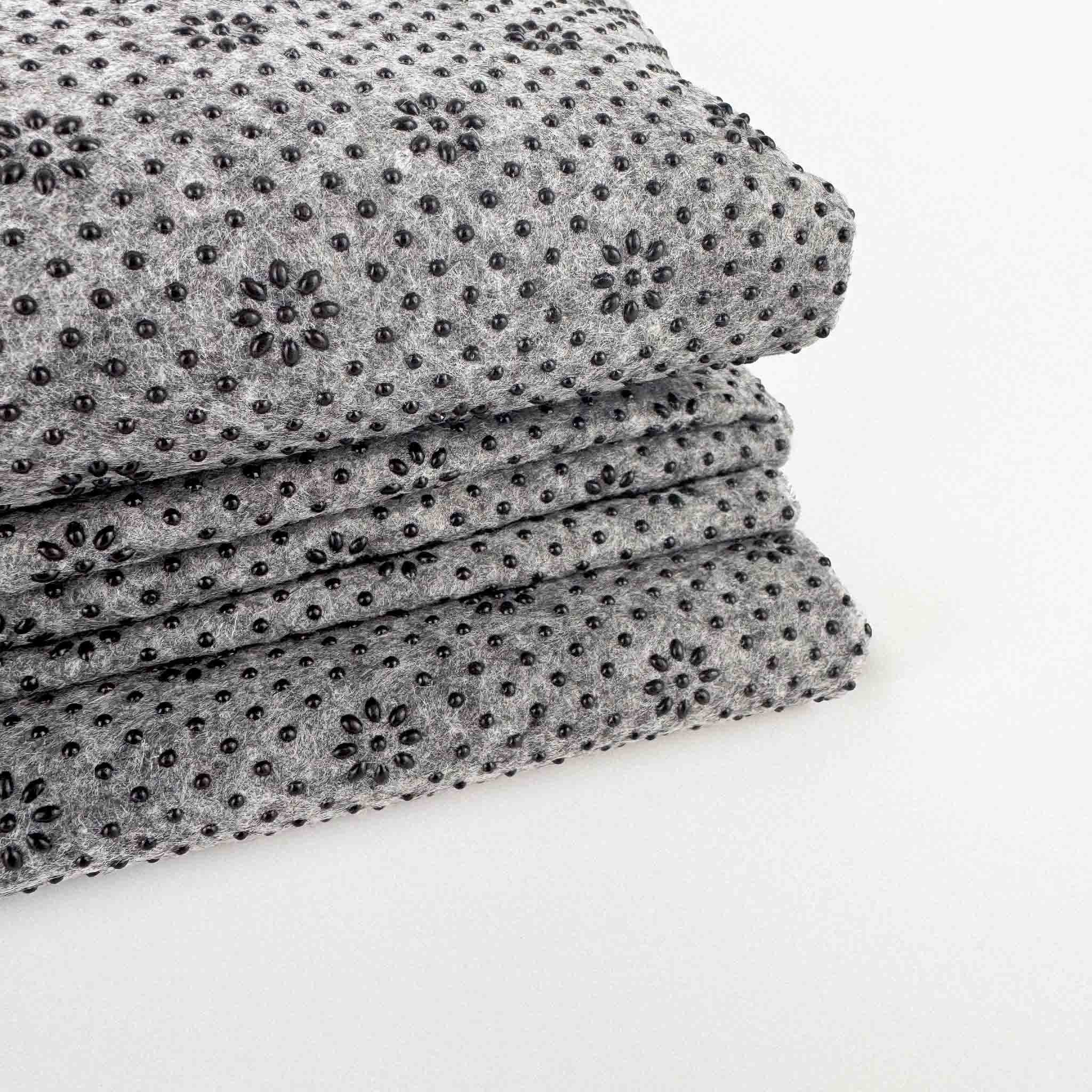 Stack of gray non slip tufting fabric with black bead silicone pattern on a white background