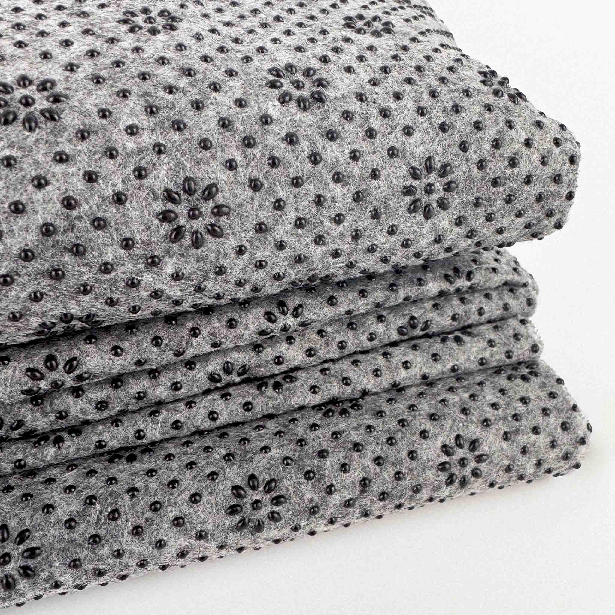 Stack of gray non slip tufting fabric with black silicone non slip beads in pattern on a white background