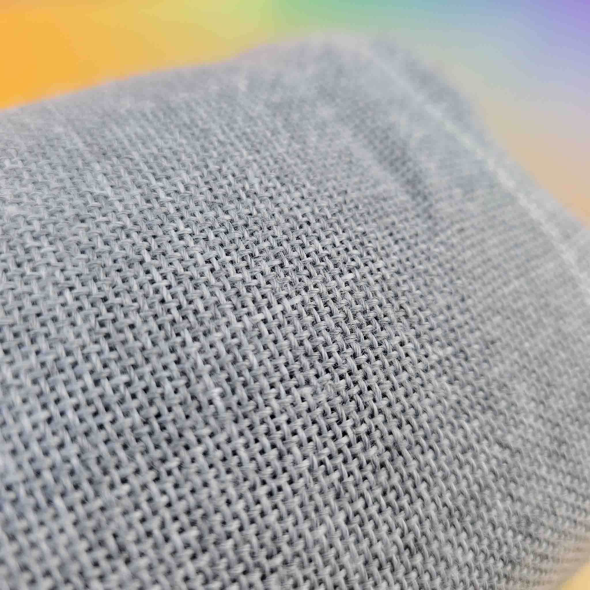 Close-up of grey woven rug tufting primary fabric with a blurred rainbow background