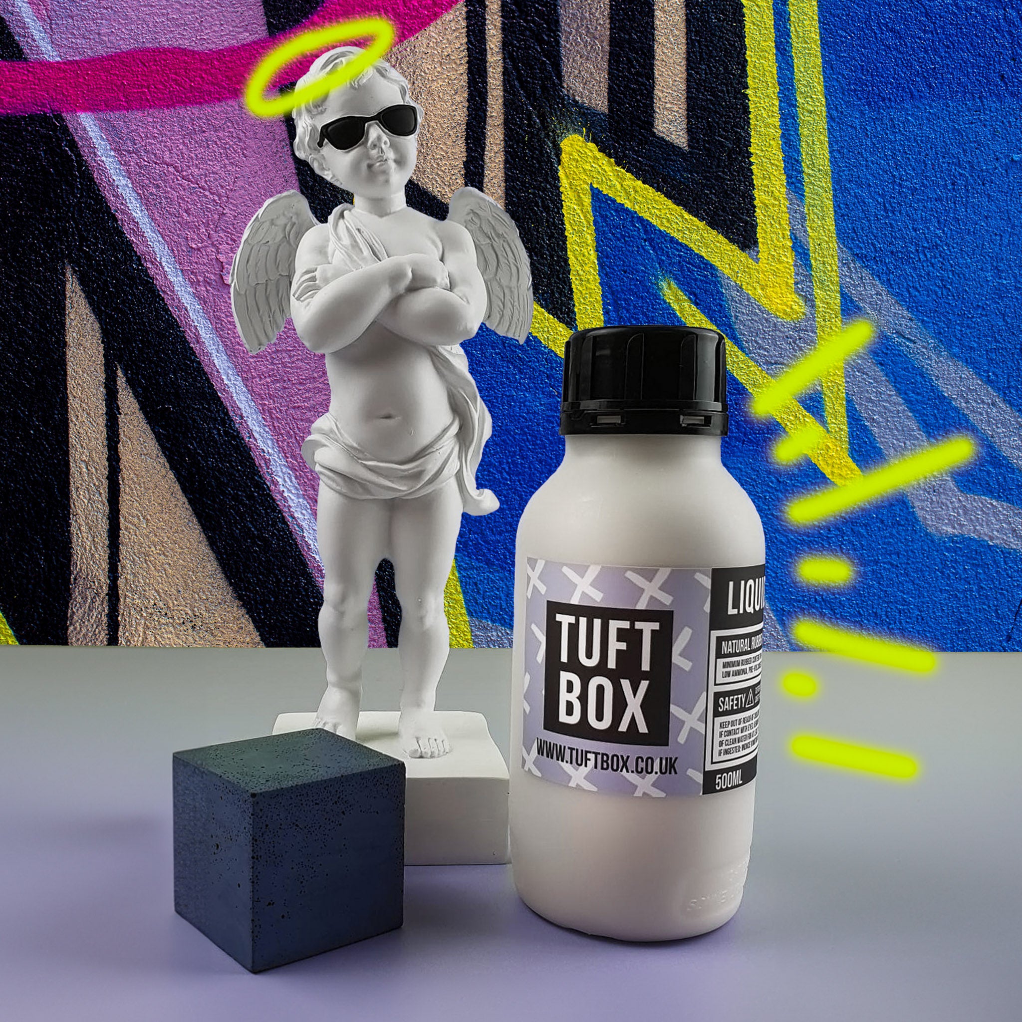 Tuftbox Liquid Latex rug glue with a small statue of a cherub with a graffiti background