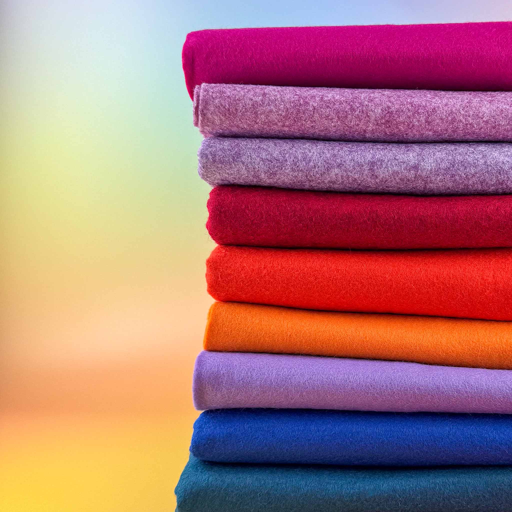 Stack of colorful felt backing fabric rolls on a gradient background