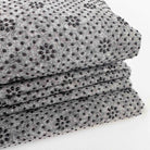Stack of gray non slip tufting fabric with black silicone non slip beads in pattern on a white background