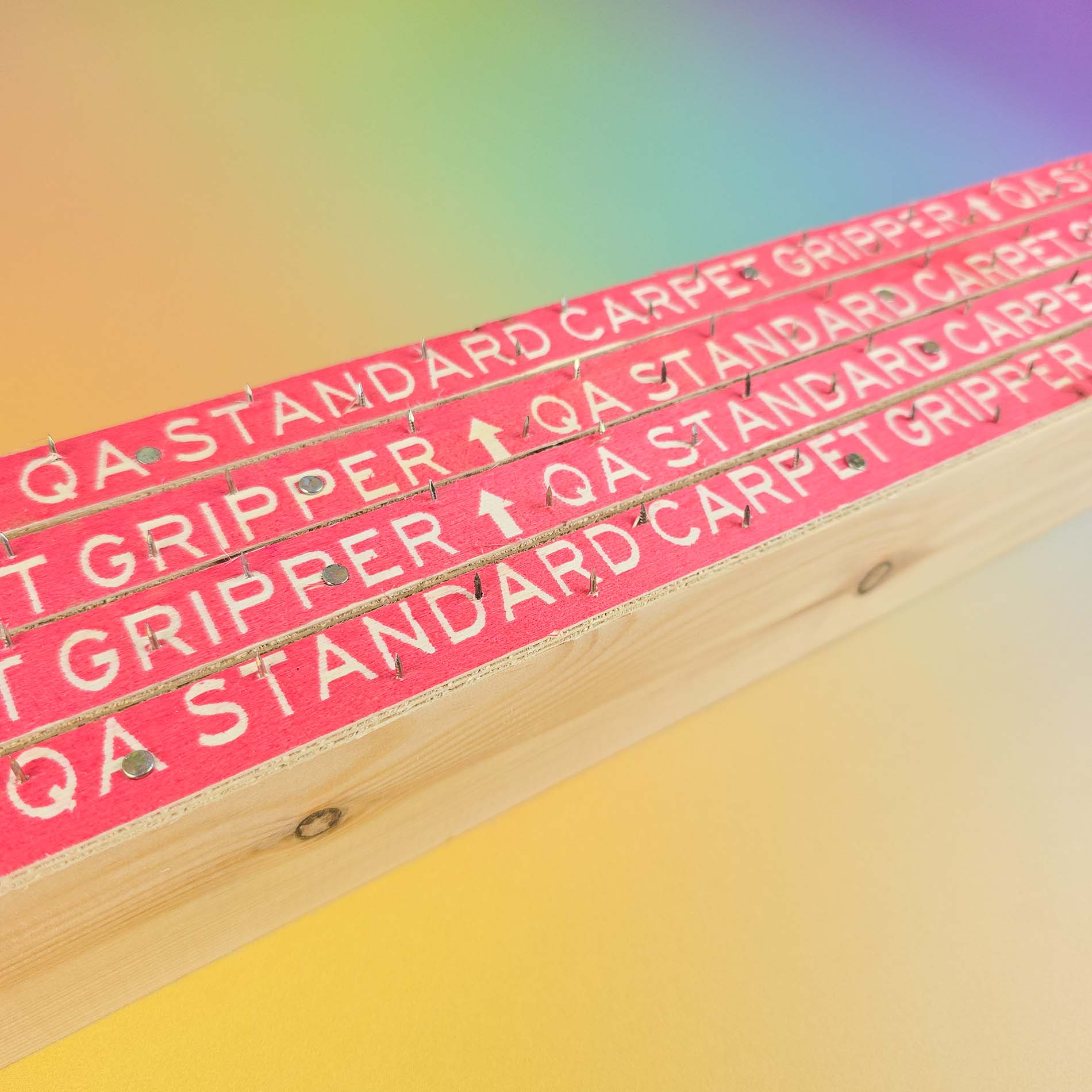 Wooden carpet gripper strips which have red text 'QA standard carpet gripper' and sharp nails on a colorful background