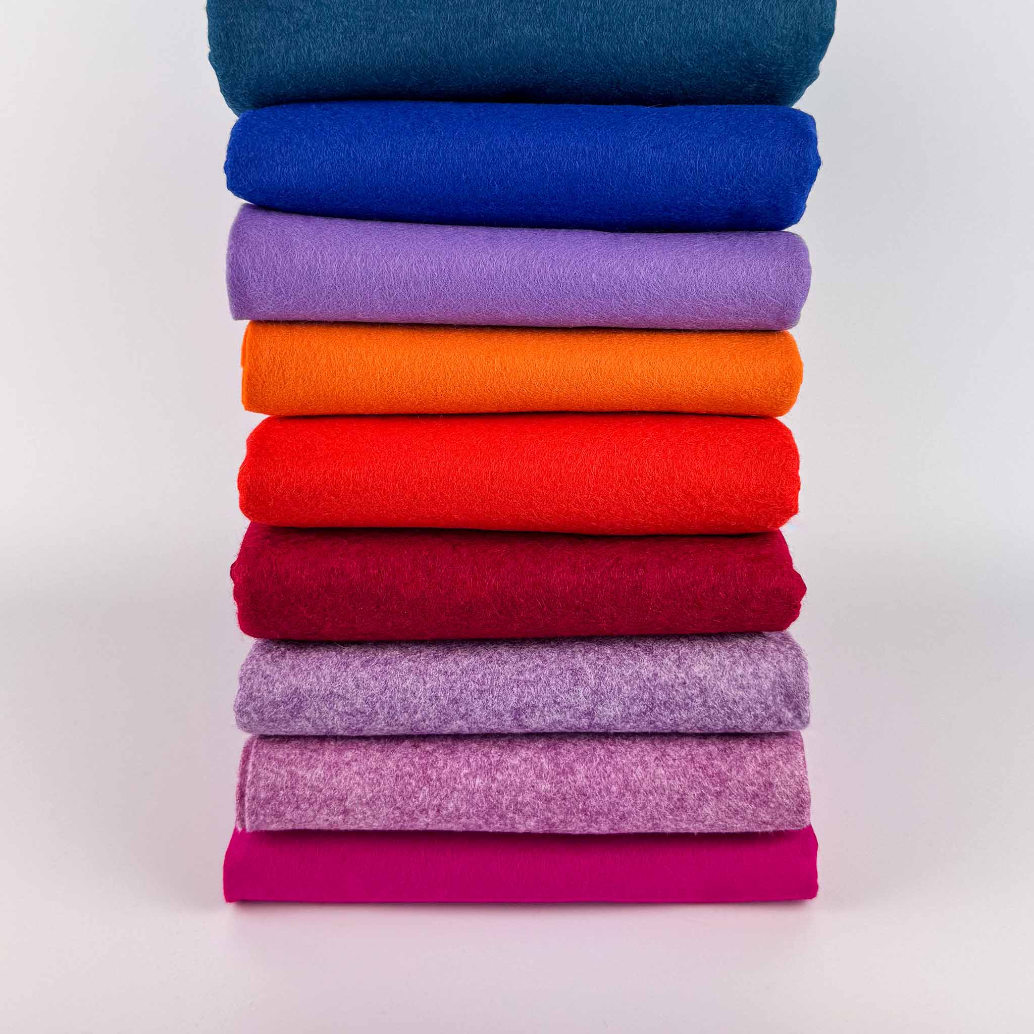 Stack of colorful folded felt backing tufting fabric on a white background